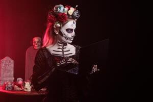Woman working on laptop during Dia de los Muertes indigenous rites of honoring the dead. Lady typing on notebook, participating in Day of the Dead, Mexico annual event in honor of the deceased photo