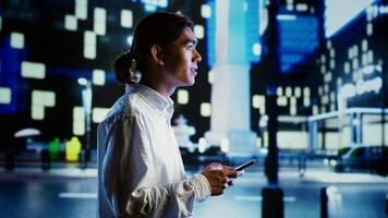 Man walking around city at night, scrolling on online shopping platform using mobile phone, blurry cityscape background. Person using smartphone while strolling on empty streets illuminated by lamps photo