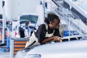 Mechanic in car service picking torque wrench from work station bench, using it to tighten bolts after replacing motor. BIPOC garage worker uses professional tools to fix client automobile photo