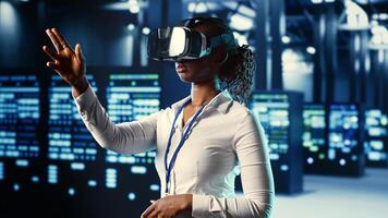 African american experienced specialist immersed in virtual reality at data center, doing units maintenance. Adept professional using VR headset to optimize servers performance, checking operations photo