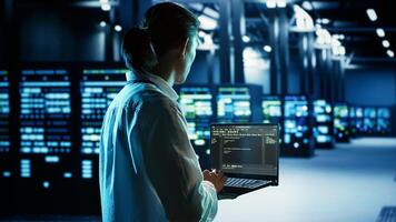 Qualified IT developer running code on laptop, troubleshooting and upgrading data center equipment designed to accommodate server cabinets, networking systems and storage arrays photo