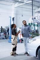 Expert in repair shop using AR technology to show man car maintenance parameters. Garage worker using futuristic vr headset to inform client of what defects his vehicle is facing photo