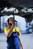 Mechanic in car service using professional mechanical tool to repair broken tires. Competent worker in garage underneath client automobile, ensuring optimal automotive performance photo