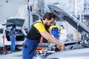 Car service technician expertly examines engine using advanced mechanical tools, ensuring smooth automotive performance and safety. Competent garage expert conducts routine vehicle checkup photo