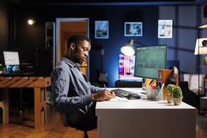 Staff worker takes notes on papers after analyzing finances, working from home on computer. African american man managing accounting analysis and financial reports online, remote work. photo