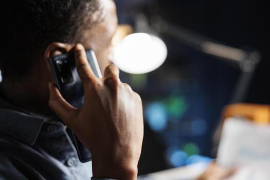 African american guy talks on phone call working from home, discusses online records with another employee. Young person contacts legal expert to chat about business accounting. photo