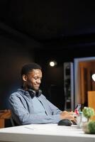 Man chatting on smartphone and listening to instructor on web based educational course, accessing social media apps and joining online class lesson. African american pupil studies at home. photo