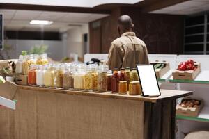 Image showcasing a digital tablet with a blank chromakey mockup template vertically positioned near glass jars. On the counter is a smart device displaying an isolated white screen. photo