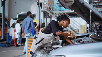 Repair shop workers using torque wrench and screwdriver to fix car in need of repairments. Colleagues servicing broken vehicle, checking for oil leakage using professional tools photo
