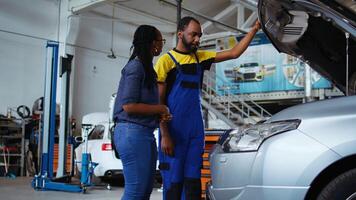 Certified serviceman listens to customer in repair shop, using tablet to write down car modifications needed. Specialist in garage workspace with client, listening to her requests for vehicle tuning photo