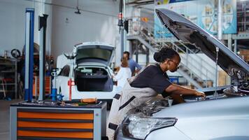 Trained serviceman in repair shop using torque wrench to tighten screws after checking car parameters during maintenance. Expert using professional tool in garage to mend vehicle, ground level shot photo