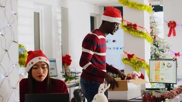 Exicted african american employee clearing desk before leaving for vacation, dancing around festive decorated office. Man wearing Santa hat taking days off to go on xmas holiday, feeling merry photo