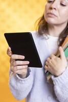 Woman carrying stack of books, reading online courses files for school exam on tablet, studio background. Student holding textbooks, doing research for university assessment on internet using device photo