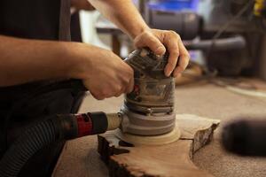 Artisan in studio enjoying diy hobby, using orbital sander with fine sandpaper on lumber to achieve smooth finish. Creative person in carpentry shop uses angle grinder to create wooden objects photo