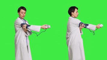 Healthcare specialist using a tonometer to measure high blood pressure and pulse, presenting tool used at checkup examinations. Doctor in white coat stands against greenscreen backdrop. Camera B. photo