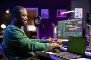 Young artist producing new tracks on daw software next to an isolated mockup screen. Sound designer composing and editing his recordings, adjust volume levels with mixing console knobs. photo