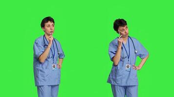 Medical assistant thinking about new treatment ideas in studio, acting thoughtful while she stands against greenscreen backdrop. Pensive young nurse contemplating about healthcare ideas. Camera B. photo
