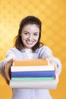 Portrait of joyous reading enthusiast woman offering stack of books, doing recommendation, isolated over studio background. Cheerful nerd giving pile of textbooks, doing endorsement photo