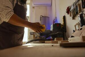 Artisan in studio using sandpaper for smoothing wooden surface, creating wood art designs. Woodworking professional using sanding sheets to refurbish damages suffered by timber block photo