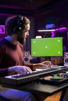 Musician learning to play electronic keyboard synthesizer in home studio, watching tutorial online via greenscreen on computer. Music composer playing midi controller notes, rehearsal practice. photo