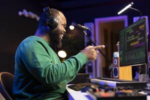 Artist songwriter feels happy with his recorded audio files in home studio, working with mixing console to compose new music. Pleased sound engineer producing creative tunes on software. photo