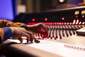 Music engineer using audio mixer and console in professional studio, adjusting volume levels while pressing switchers and twisting knobs on control board. Technician works with buttons. Close up. photo