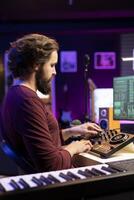 Young musician composing soundtracks and editing them on mixing console, creating cool tunes on daw software interface in his home studio. Producer adjusting volume levels on stereo gear. photo
