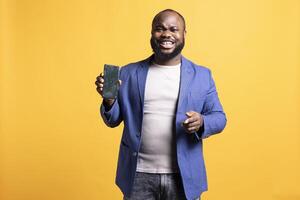 Overjoyed african american influencer presenting green screen mobile phone, isolated over studio background. Joyful BIPOC person holding copy space chroma key smartphone used for advertising brands photo