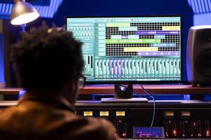 African american sound engineer recording music and working with digital audio software on pc, editing in post production. Mixing and mastering expert twisting knobs and buttons. photo