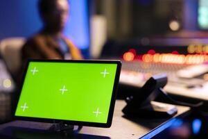 African american audio technician editing tracks next to isolated display on tablet, operating on control room panel board. Music engineer pushing faders and buttons in post production studio. photo
