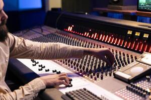 Audio editor changes and blends records to create fresh tracks, adding sound effects to boost audio recordings quality. Music production expert working in professional studio control room. photo