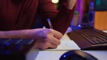 Composer developing an original track In his home studio, writing down lyrics and harmonic notes before recording the song melody. Musician using DAW computer apps for creating music. Camera B. photo
