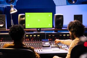 Team of specialists recording and editing tracks with isolated screen on pc, working on a new album and creating songs. Audio engineer operating mixing console with motorized faders. photo