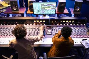 Audio expert and singer collaborating on music for new album, composing and editing tracks with mixing console and digital software on pc. Artist working with producer for cool records in studio. photo