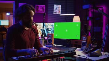 Musician playing piano midi controller and learning new notes, looking at online lesson on pc. Artist uses greenscreen display, learn to play keys on electronic keyboard. Camera B. photo