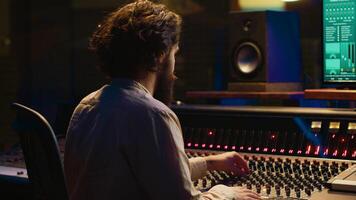 Mixing engineer focuses on blending and balancing individual tunes of a recording to create song, audio editing software in control room. Expert deals with technical aspects of sound. Camera A. photo