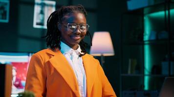 Portrait of african american student putting glasses on and working on english essays at home, reading academic databases for additional resources. Young woman studying at university. Camera A. photo