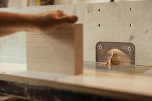 Man putting lumber block through spindle moulder, creating smooth and precise edges on wooden pieces. Joiner using heavy machinery to craft strong and seamless joints for furniture and structures photo