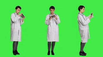 General practitioner playing games on mobile phone app, having fun with online gaming competition against greenscreen backdrop. Cheerful doctor relaxing with internet game. Camera A. photo
