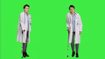 Orthopedics specialist presenting walking tool after fracture or injury, showing crutches to help with recovery. Physician stands against greenscreen backdrop, mobility aid. Camera A. photo