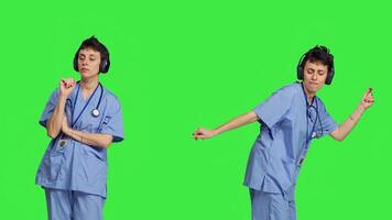 Cheerful health specialist listening to cool music on audio headset, dancing against greenscreen backdrop and having fun. Nurse enjoying songs an doing funny dance moves, leisure. Camera B. photo