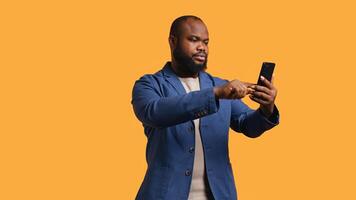 Smiling african american man greeting friends during teleconference meeting using smartphone, studio background. Friendly person waving hand, saluting mate during internet call, camera B photo