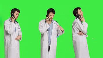 Woman doctor talking on smartphone call against greenscreen backdrop, answering phone line to make an exam appointment for a patient. Physician uses mobile phone to chat with people. Camera B. photo