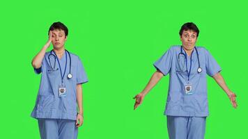 Medical assistant having a headache and doing confusion symbol, standing against greenscreen backdrop. Nurse deals with a migraine and burnout, shows i dont know sign and being clueless. Camera B. photo