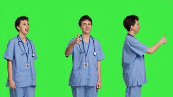 Cheerful nurse giving thumbs up sign against greenscreen backdrop, showing positive gesture with a like. Medical assistant shows her approval, recommending something and being satisfied. Camera B. photo