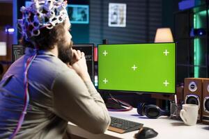 Neuroscientist using EEG headset to upload his mind into green screen computer, attaining immortality. Software developer using mockup PC, experimenting with transferring consciousness into cyberspace photo