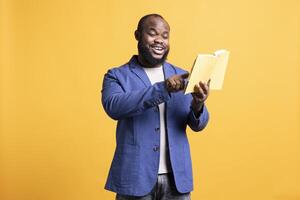 Cheerful man reading interesting book, pointing finger to favorite part on page. Joyous person having fun enjoying literature novel during leisure time, isolated over studio background photo