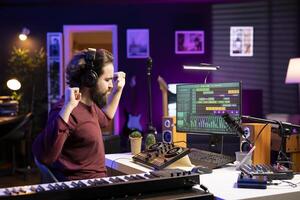 Please happy songwriter creating new music on daw software, using headset to listen to the final product in home studio. Young music producer editing audio files recordings on pc. photo