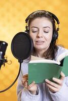 Smiling caucasian person doing voiceover of book, producing audiobook. Merry narrator using storytelling skills while producing digital recording of novel, isolated over studio background photo