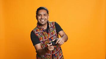 Happy gamer celebrating after winning game on gaming console, studio background. Delighted Indian man bragging after being victorious in videogame, defeating all enemies using gamepad, camera B photo
